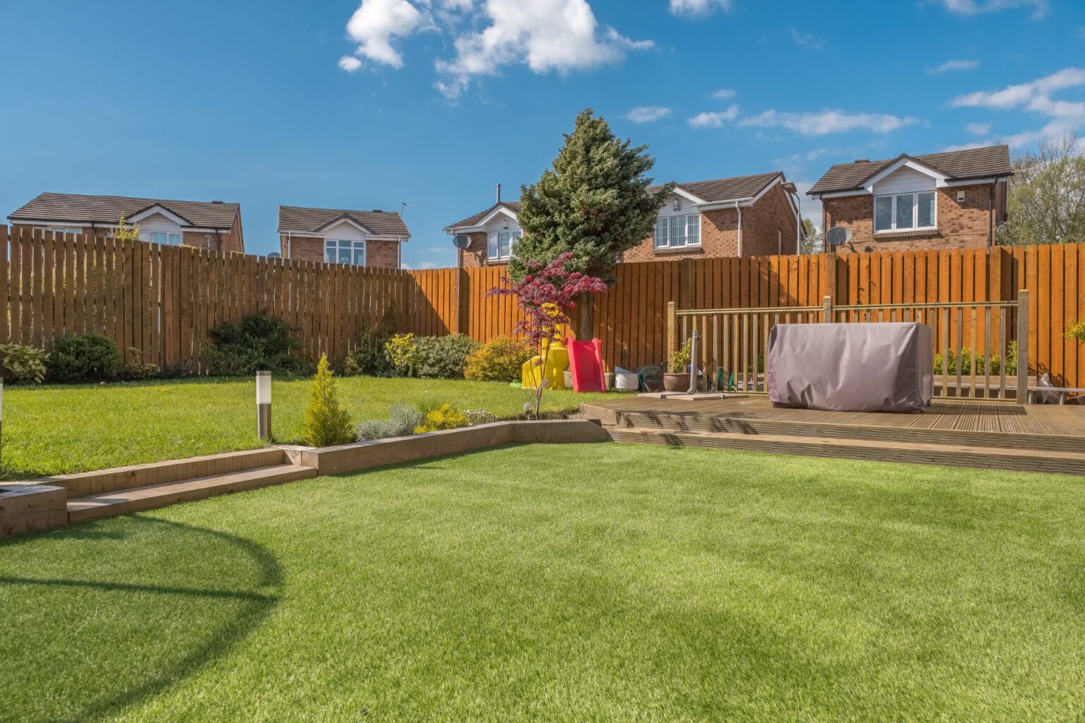 A newly completed and replanted landscaped garden with mixer of artificial and natural sown grass, new borders planted, a new decking patio and garden ornaments surrounded by new erected wooden fencing all to a modern design. A good image for a landscape gardener designer or garden retail centre.